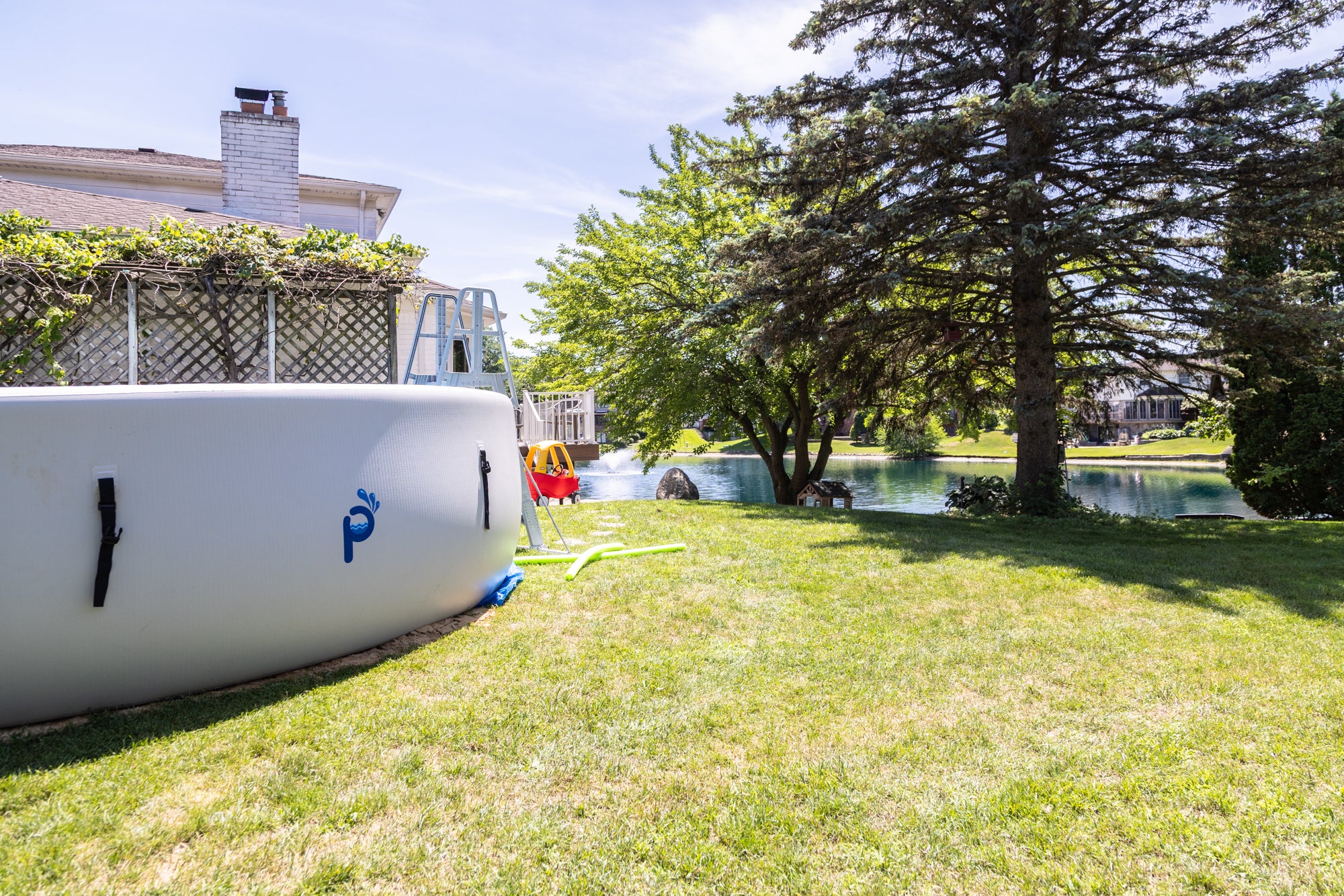 Perfect Pools above‑ground pool set up in a lush backyard beside a lake, with a ladder and children’s play equipment, illustrating the lifestyle around the brand