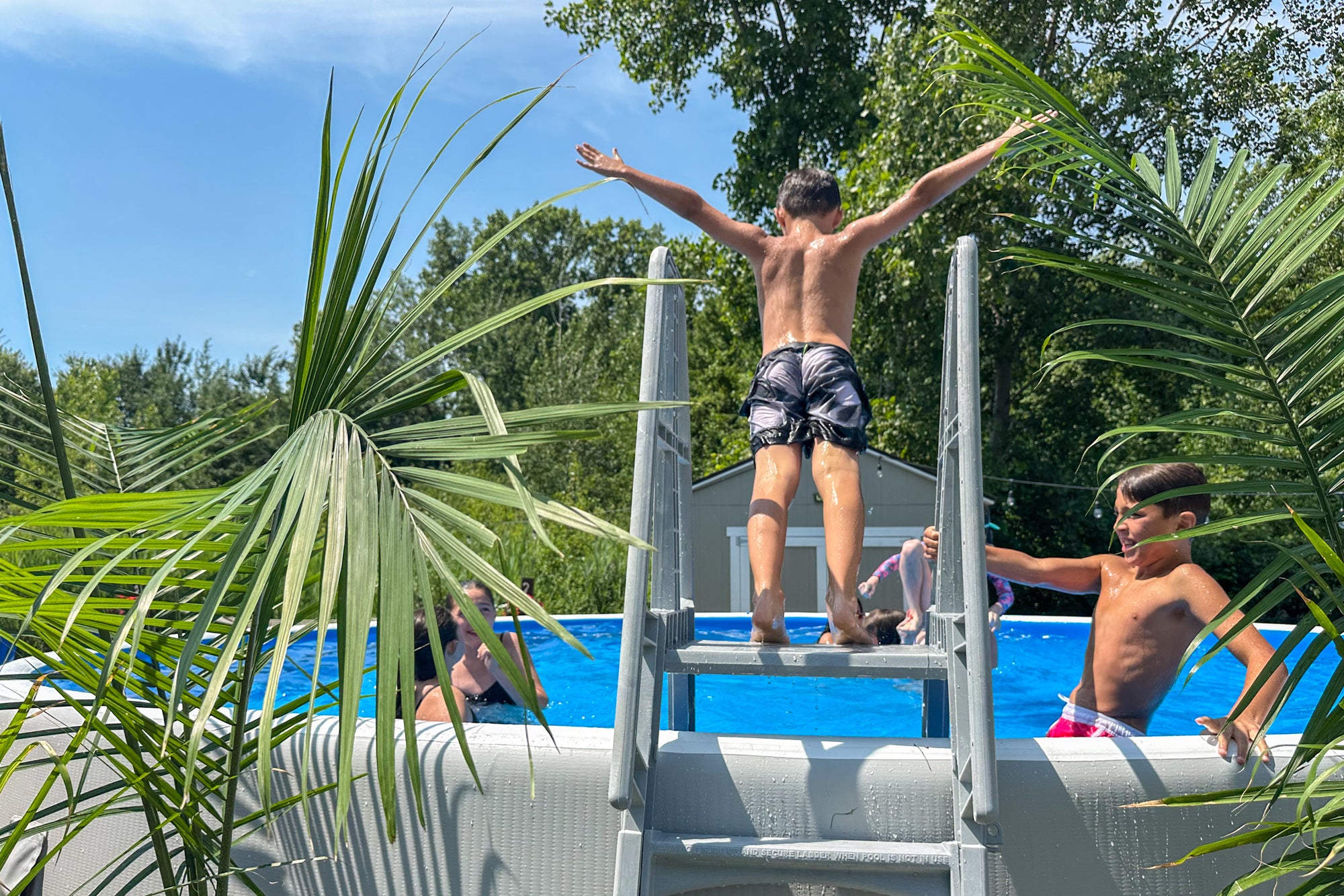 Boy standing on a Perfect Pool ladder with arms raised, preparing to jump into the pool on a sunny day