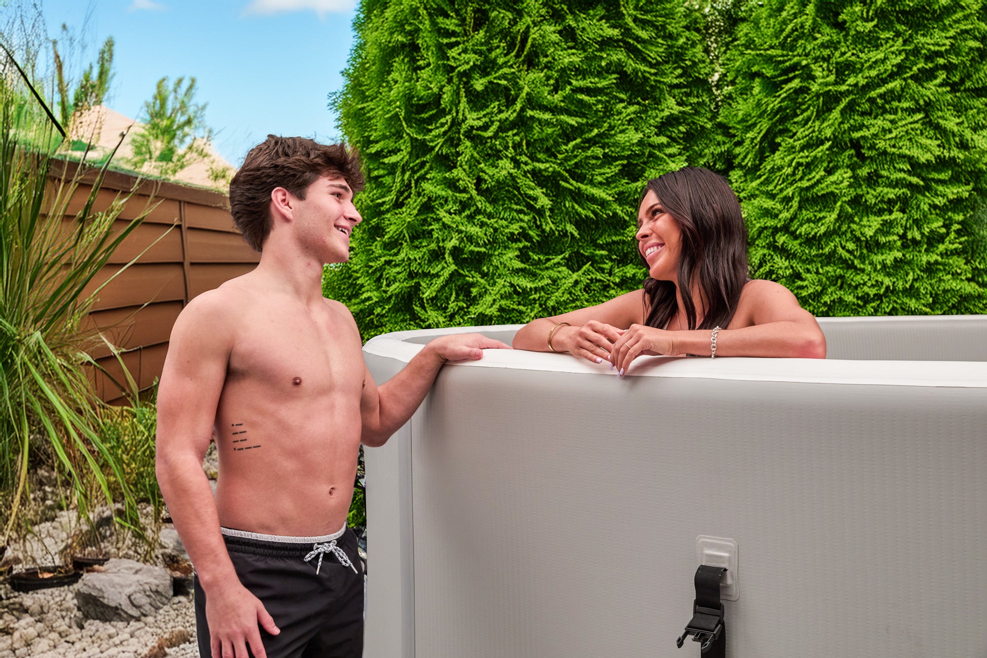 Young couple chatting and leaning on a Perfect Pool drop‑stitch pool with lush greenery in the background, illustrating social relaxation