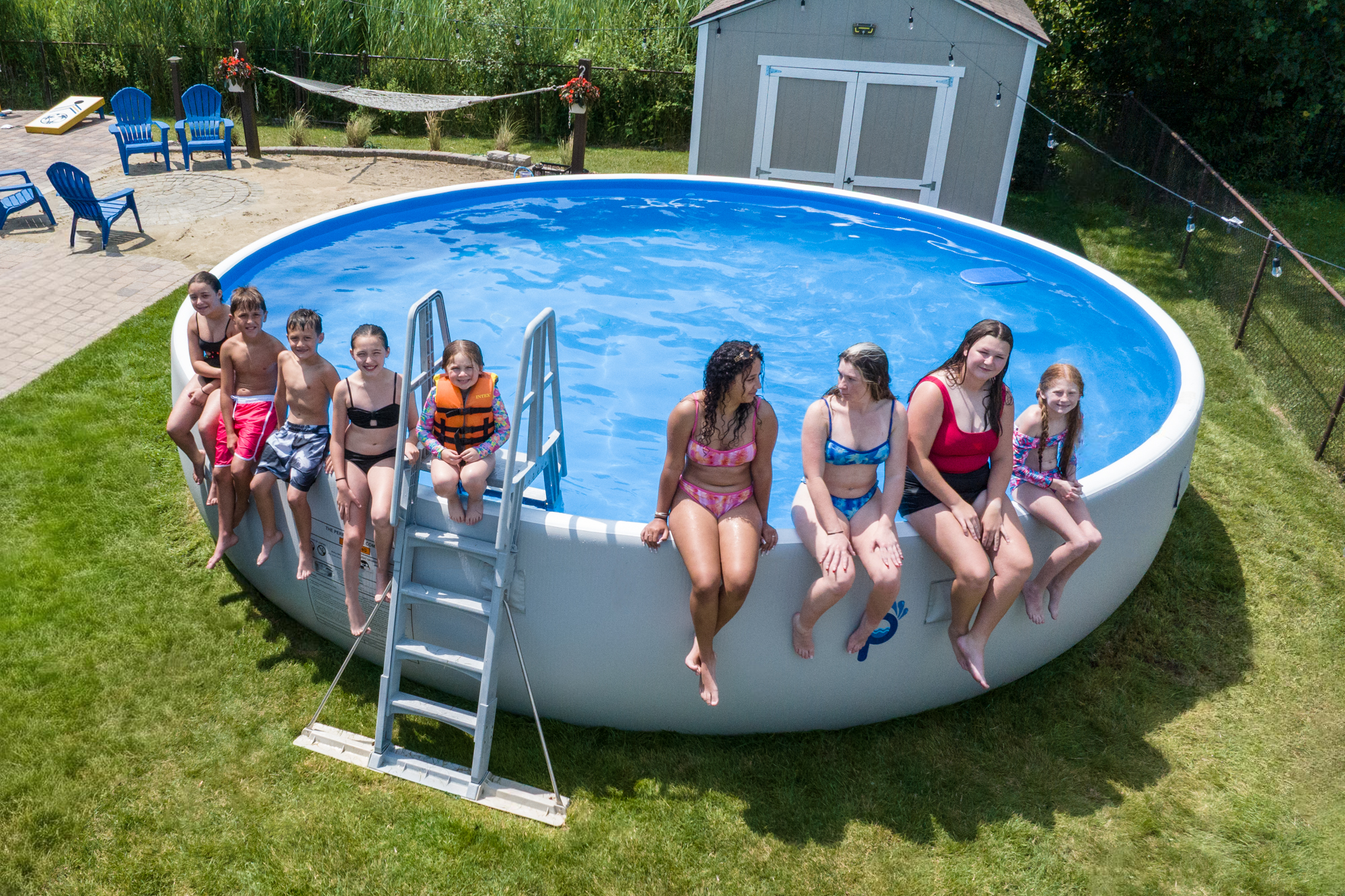 Large family sitting on the rim of a Perfect Pool set up on grass, showcasing how the pool accommodates many swimmers after simple installation